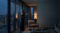 Professional businesswoman standing by floor-to-ceiling windows in modern office overlooking city skyline at dusk, contemplating success and future opportunities.