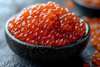 Fresh red caviar in black ceramic bowl, macro shot showing detailed texture of salmon roe pearls against dark background. Luxury seafood delicacy.