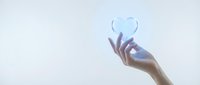 Hand holding glowing blue heart symbol against soft light background representing love, care, healthcare, charity and emotional wellness concepts.