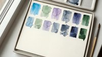 Watercolor paint palette with mixed blue, green and purple colors in art supplies box with brushes for creative painting and artistic projects.