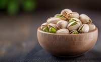 Fresh roasted pistachio nuts in wooden bowl on dark rustic table background, healthy snack with natural green kernels, macro food photography.