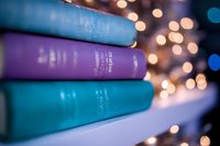 Stack of colorful hardcover books against blurred bokeh lights background, creating cozy reading atmosphere with purple and turquoise spines in soft focus.