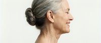 Senior Caucasian woman with gray hair in bun smiling in profile showing natural aging and confidence on neutral background for wellness campaigns.