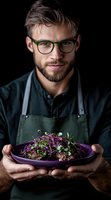 Beard presenting gourmet dish with microgreens and sprouts on purple plate against dark background. Professional food service portrait.