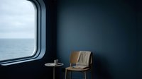Minimalist interior with wooden chair and small table beside porthole window overlooking calm sea, conveying solitude and maritime tranquility for design and lifestyle projects.
