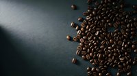 Roasted coffee beans scattered on dark textured surface, overhead view for beverage, café, and food industry design projects.