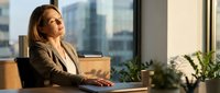 Professional businesswoman contemplating future plans while working at modern office desk with city skyline view during golden hour lighting.