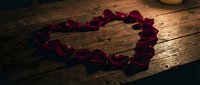 Heart shape made of red rose petals on rustic wooden table in candlelight, romantic mood for Valentine's Day or anniversary celebration.