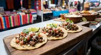 Three authentic Mexican tacos with seasoned meat, fresh cilantro, diced onions and lime wedges served on corn tortillas arranged on rustic wooden board in restaurant.
