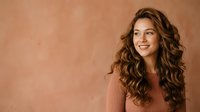 Young woman with long wavy brown hair and fair complexion smiling against warm beige background, suitable for beauty, lifestyle, and portrait projects.