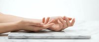 Female hands in relaxed meditation pose resting on marble surface against clean white background for wellness and mindfulness concepts.