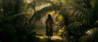 Young woman with long dark hair, wearing casual clothing, standing alone in a lush jungle environment surrounded by dense tropical vegetation and palm fronds, with golden sunlight filtering through the canopy creating atmospheric lighting.