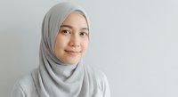 Young Muslim woman wearing gray hijab smiling confidently against neutral background for professional business portrait and lifestyle content.