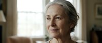 Senior woman with gray hair and fair complexion, appearing thoughtful and serene indoors near natural window light, suitable for healthcare, wellness, aging, and lifestyle editorial use.