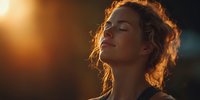 Young woman with curly hair enjoying peaceful moment in warm golden sunlight with eyes closed, expressing serenity and mindfulness during sunset hour.