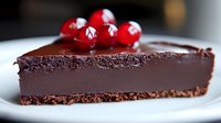 Rich dark chocolate tart slice garnished with fresh red currants on white plate, showcasing smooth ganache texture and crisp chocolate crust base.