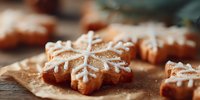 Gingerbread snowflake cookies with white icing decoration on parchment paper, festive holiday baking for Christmas celebrations and winter treats.
