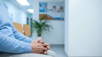 Elderly person sitting with clasped hands in a bright hospital waiting room, conveying patience, anxiety, and healthcare themes.