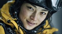 Close-up portrait of young Asian woman in yellow winter jacket and ski helmet with snow flakes on face, outdoor winter sports concept.