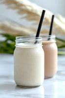 Fresh vanilla and strawberry milkshakes served in mason jars with black straws on marble surface, soft natural lighting creates appetizing drink photography.
