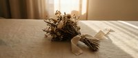 Dried flower bouquets with ribbon on white bedding in warm sunlight creating peaceful bedroom decor atmosphere for relaxation and interior design.
