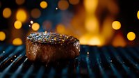 Juicy grilled beef steak with seasoning on black grill grates against warm bokeh background. Close up view of medium rare meat with golden lights.