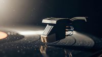 Professional turntable stylus needle on vinyl record with dramatic lighting and dust particles creating atmospheric music production scene.