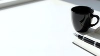Clean white desk workspace with black coffee mug and elegant pen ready for business planning, writing, or creative work in modern office setting.