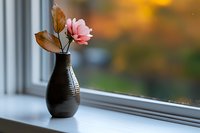 Single pink rose with brown leaves in dark textured vase on windowsill. Soft blurred background with natural light. Suitable for home decor, interior design, and lifestyle content.