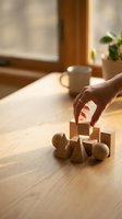 Hand arranging wooden geometric blocks on table in warm sunlight with coffee cup creating cozy morning atmosphere for learning and development activities.