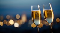 Two champagne flutes filled with sparkling wine against blurred city lights background creating romantic evening atmosphere with golden bokeh effect.