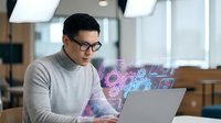 Asian businessman with glasses working on laptop with digital holographic interface displaying futuristic technology concepts in modern office environment.