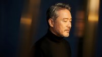 Mature Asian businessman in black turtleneck with closed eyes in contemplative pose against warm bokeh background for corporate wellness concepts.