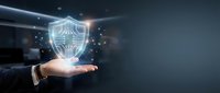 Businessman hand holding glowing shield icon with digital particles, representing cybersecurity, data protection, and network security solutions for business technology.