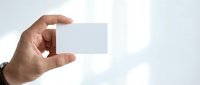 Hand holding blank white business card mockup against soft blurred background for corporate branding and professional identity design presentation.