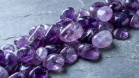 Purple amethyst gemstone beads arranged on textured slate surface for jewelry making and crafting projects.