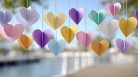 Colorful paper hearts hanging on strings create romantic decoration against blurred coastal background for wedding celebrations and love themes.