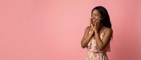 Young African American woman in floral dress talking on smartphone against pink background, smiling happily during phone conversation for communication.