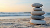 Balanced zen stones stack on sandy beach at sunset with ocean waves in background, creating peaceful meditation and wellness atmosphere.