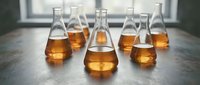 Laboratory flasks filled with amber liquid arranged on gray surface, suitable for science, chemistry, research, and educational content.