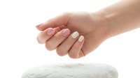 Female hands with pink and white manicured nails positioned above white towel on isolated background for spa and beauty treatments.