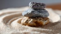 Stacked zen stones on fine sand creating peaceful balance and harmony, soft focus macro photography with shallow depth of field and warm lighting.