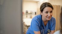 Middle-aged Caucasian female nurse in blue scrubs with stethoscope smiling warmly in modern hospital setting for healthcare and medical professionals.