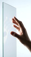 Hand touching transparent glass panel against white background, demonstrating touch interface technology for digital design, app development, and interactive user experience concepts.