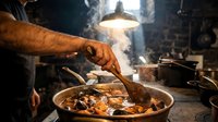 Professional chef cooking traditional stew in rustic kitchen with wooden spoon, steam rising from pan in atmospheric lighting for culinary content.