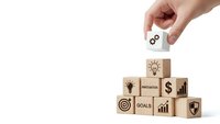 Hand placing wooden cube with gears icon completing business strategy pyramid with innovation goals target growth symbols isolated white background.