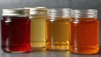 Assortment of honey varieties in glass jars showing different colors from dark amber to light golden, showcasing natural sweetener options.