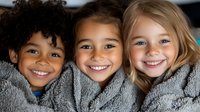 Diverse group of cheerful children wrapped in cozy gray blanket showing genuine smiles and friendship, representing unity and joy in childhood.