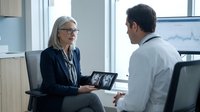 Professional blonde businesswoman in glasses consulting with male colleague using tablet in modern office meeting room for corporate strategy discussion.
