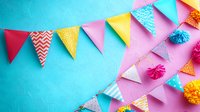 Festive paper bunting with colorful triangular flags and decorative pom-poms against split pink and turquoise background creates cheerful party atmosphere.